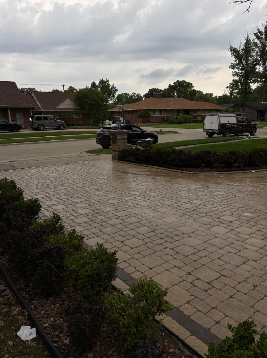 Wide tumbled cobblestone paver driveway with a wet finish, edged with a charcoal border course and a brick pillar at the street