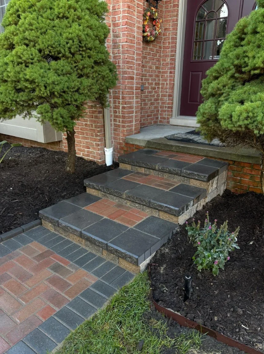 Front entry steps with charcoal capped treads leading down to a brick paver landing and walkway, bordered by fresh mulch beds