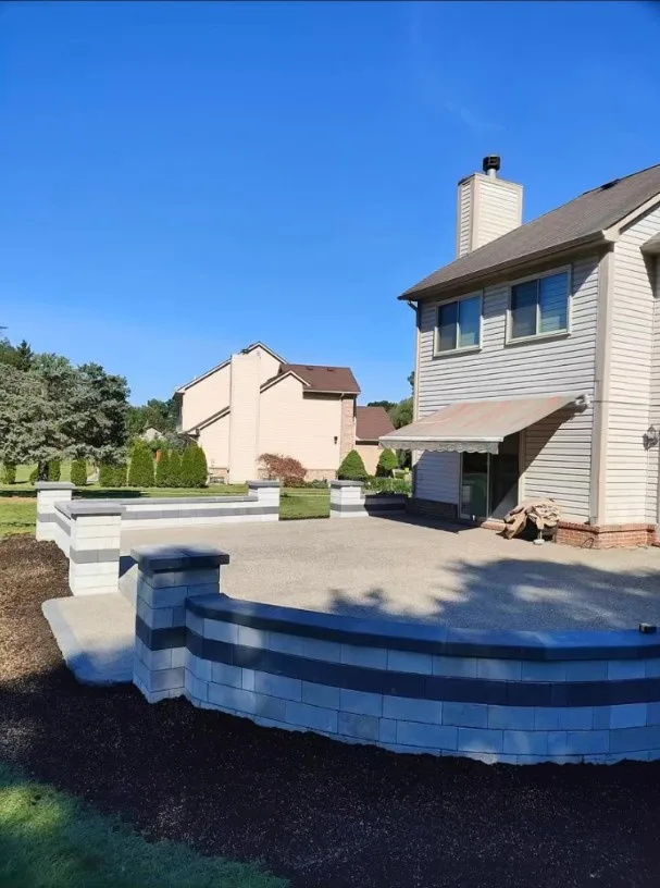 Curved gray block seating wall built around a raised patio, with the compacted aggregate base laid in behind it at a two-story home
