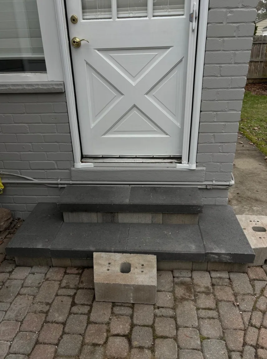 Gray stone entry steps and landing at a white service door, set above a tumbled cobblestone paver apron on a painted brick home